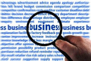 Person holding magnifying glass over the word 'business'.