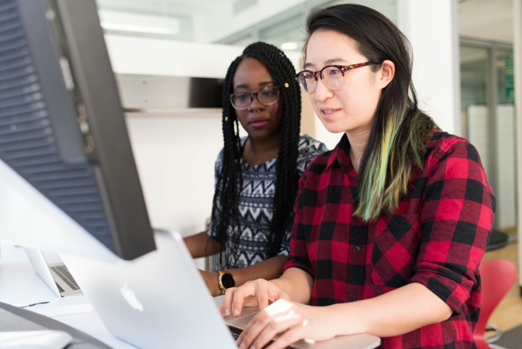 Duas mulheres usando seus computadores para descobrir como realizar uma verificação de integridade.