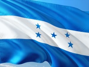 A imagem mostra a bandeira nacional de Honduras. Ela consiste em três faixas horizontais de igual largura, com faixas azuis na parte superior e inferior e uma faixa branca no meio. No centro da faixa branca há cinco estrelas azuis dispostas em um padrão, simbolizando a unidade - um aspecto fundamental ao fazer negócios em Honduras.