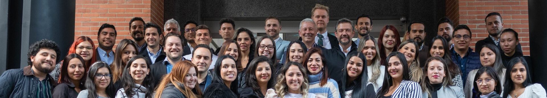 BLH Team The biz latin hub team, stand closely together in front of a building with brick walls. They are dressed in a variety of outfits ranging from casual to business attire.