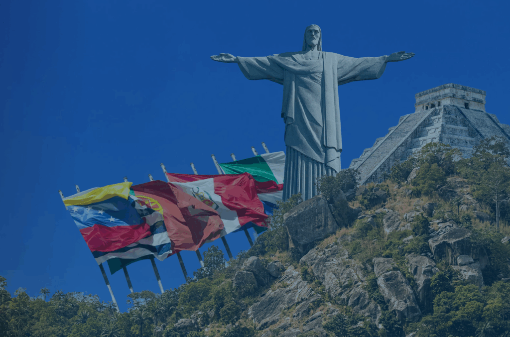 Header homepage BLH A large statue of Christ the Redeemer stands on a rocky hill, surrounded by greenery. Several national flags, including those of Venezuela, Peru, Brazil, and Argentina, are displayed to the left of the statue. The clear blue sky frames this iconic landmark seamlessly into its picturesque setting.